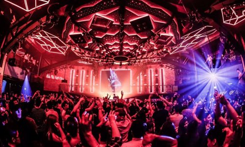 DJ performing at an Asian techno club with neon lights and crowd